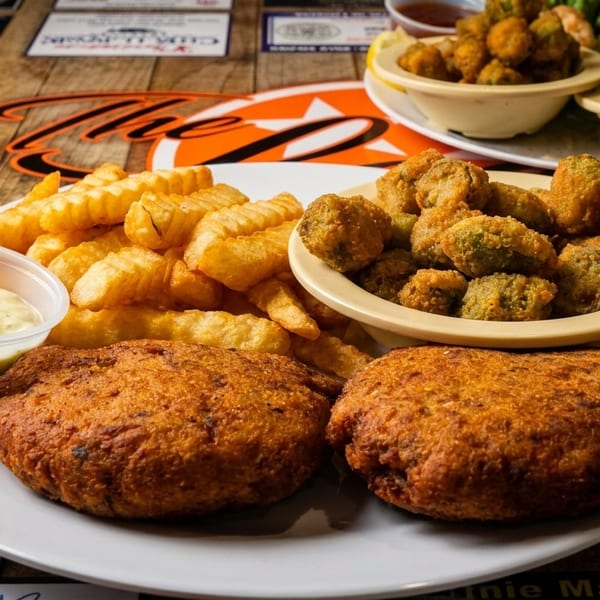 Fried seafood patties, crinkle-cut fries, and fried okra with tartar sauce on a wooden table.