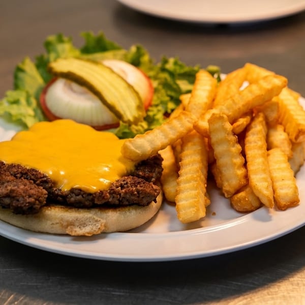 Cheeseburger with melted cheese, crinkle-cut fries, lettuce, onion, and pickles on a white plate.